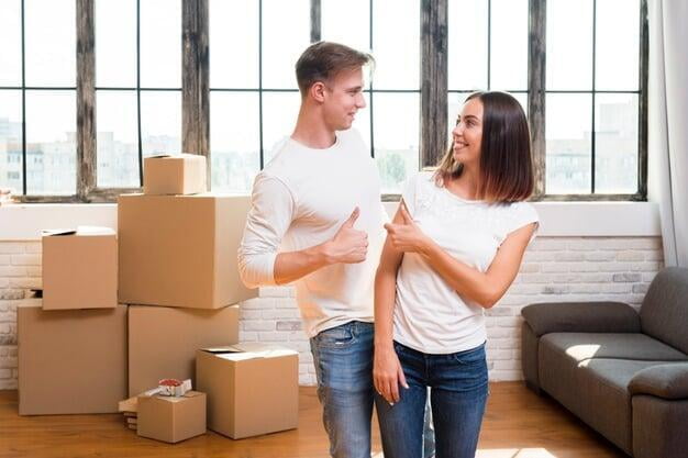 Photograph of a happy young couple in a room with packed boxes.  Looks like they just moved into their new house!