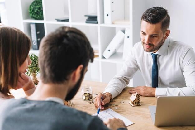 Photograph of a real estate agent sitting at a desk with a couple going over paperwork